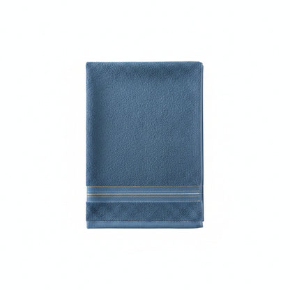 A blue cotton towel with a decorative gold stripe border draped over the back of a wooden cane chair.