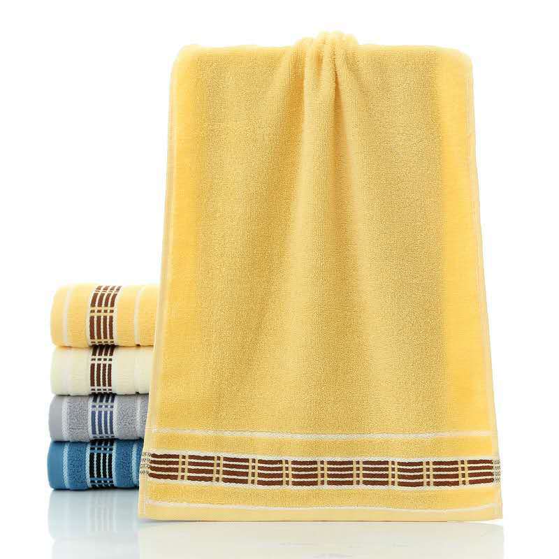 Yellow towel with decorative hem, stacked with other towels on a white background
