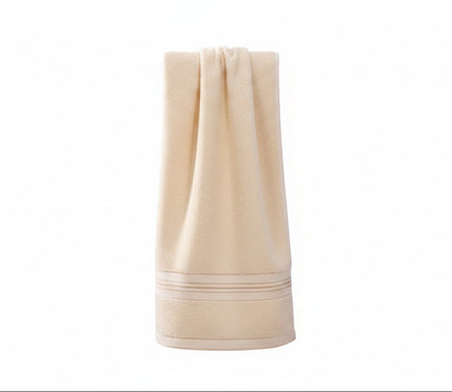 A beige cotton bath towel with a stitched border sits draped over a wooden chair.